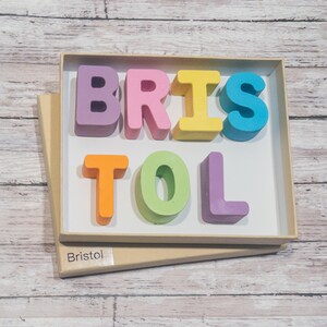 May include: A wooden box with the name "Bristol" spelled out in colorful letters. The letters are in a variety of colors, including pink, purple, yellow, orange, green, and blue.