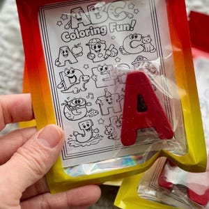 May include: A red letter "A" in a clear plastic package, with a coloring book page behind it. The coloring book page has the text "ABC Coloring Fun!" and illustrations of letters and objects.