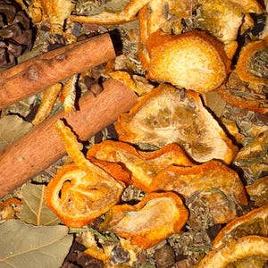 May include: Close-up of a collection of dried orange slices, cinnamon sticks, bay leaves, and various spices. The arrangement includes small pine cones and peppercorns, creating a warm, earthy aesthetic. The colors are predominantly orange, brown, and green.