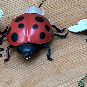 May include: A red and black ladybug toy with a green wire tail. The ladybug is on a wooden surface.