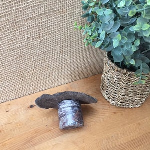 May include: A camouflage-patterned cylindrical container with a brown, textured lid. The container is sitting on a wooden surface.