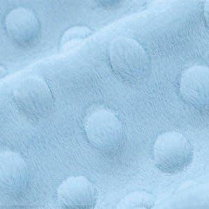 May include: Close-up of a light blue fabric with a textured pattern of small, raised circles.