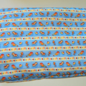 May include: Blue fabric with a repeating pattern of a rocking horse, a toy truck, a toy boat, and a toy fire truck. The pattern is on a white background with blue stripes. The fabric has the text "abc 123" repeated throughout.