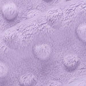 May include: Close-up of a soft, lavender-colored fabric with a textured, plush surface. The fabric has a raised, dotted pattern, creating a tactile and visually appealing texture. The material appears to be a cozy, warm textile.