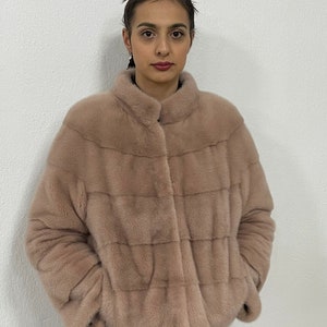 K&ouml;nnte beinhalten: Eine hellrosa Kunstfelljacke mit Rei&szlig;verschluss. Die Jacke hat einen Stehkragen und ist tailliert.