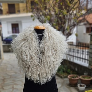 Peut inclure: Un col en fausse fourrure blanc et moelleux avec de longues mèches hirsutes. Le col est présenté sur un mannequin noir.