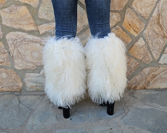 May include: White fluffy faux fur leg warmers with a black heel. The leg warmers are worn over jeans.