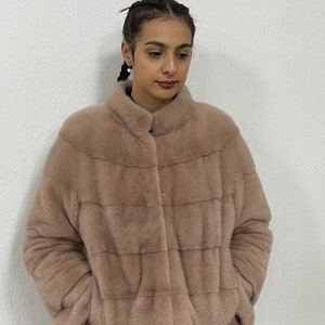 K&ouml;nnte beinhalten: Eine hellrosa Pelzjacke mit Rei&szlig;verschluss. Die Jacke hat einen Stehkragen und ist taillenkurz.