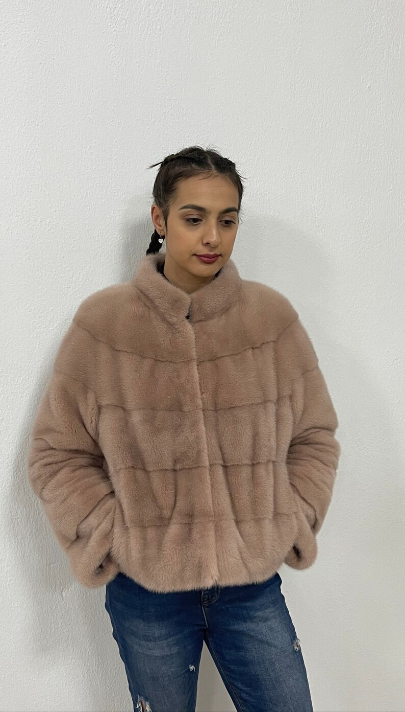 K&ouml;nnte beinhalten: Eine hellrosa Pelzjacke mit Rei&szlig;verschluss. Die Jacke hat einen Stehkragen und ist taillenkurz.