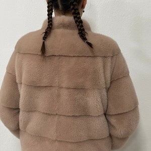 K&ouml;nnte beinhalten: Eine hellbraune Pelzjacke mit Stehkragen und Rei&szlig;verschluss. Die Jacke ist aus weichem, luxuri&ouml;sem Pelz gefertigt und hat eine lockere Passform.