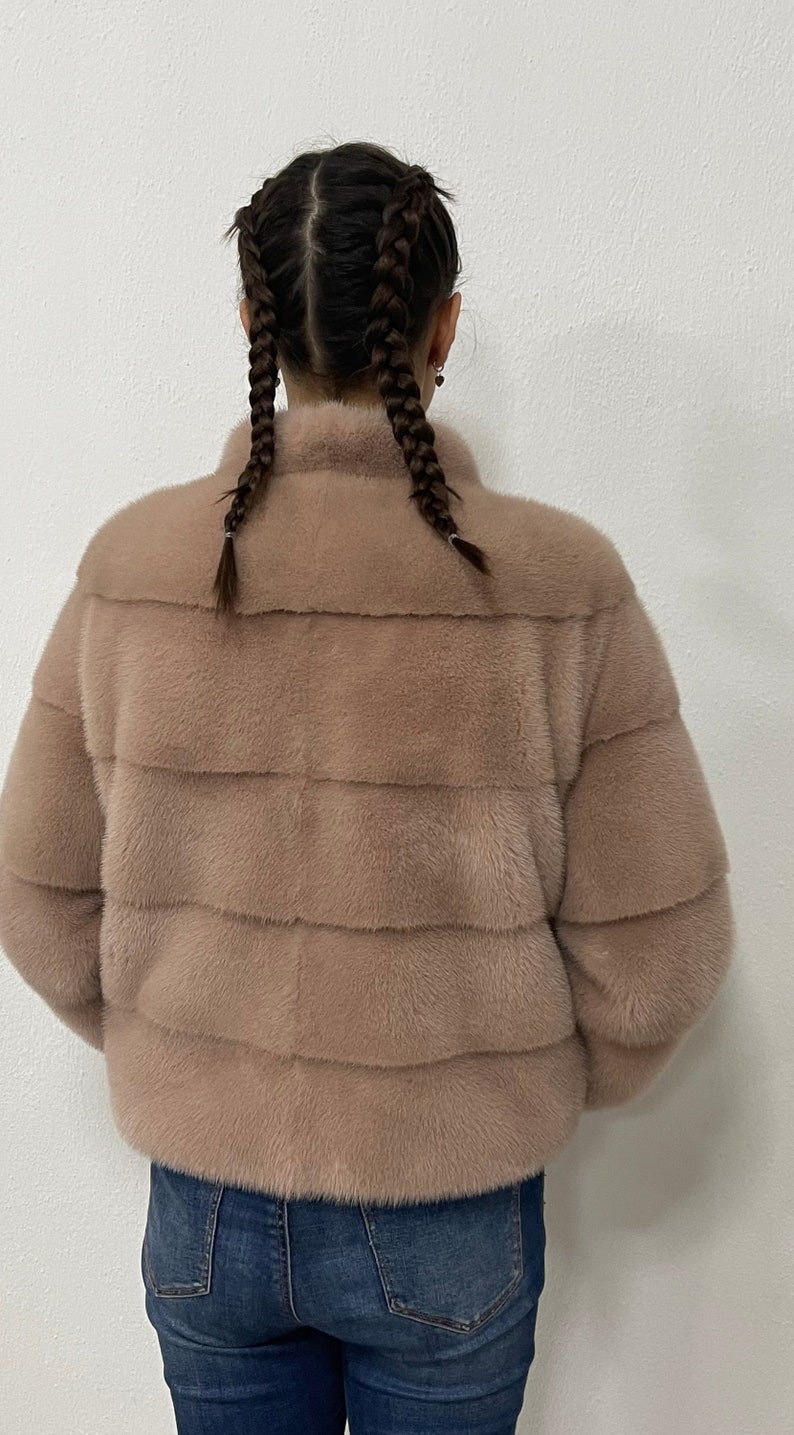 K&ouml;nnte beinhalten: Eine hellbraune Pelzjacke mit Stehkragen und Rei&szlig;verschluss. Die Jacke ist aus weichem, luxuri&ouml;sem Pelz gefertigt und hat eine lockere Passform.