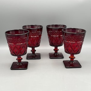 May include: Four ruby red vintage goblets. Each glass features a square base, a short stem, and a diamond pattern on the bowl. The rims have a textured design. These glasses are perfect for serving wine or other beverages.