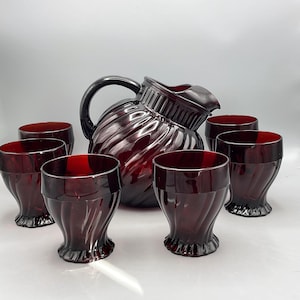 May include: A vintage ruby red glass pitcher and matching glasses set. The pitcher has a large handle and a spiral design. The glasses have a similar spiral design. The set is perfect for serving beverages.