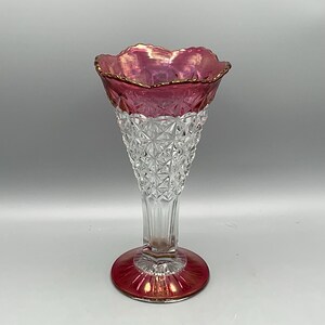 May include: A clear glass vase with a flared, ruffled top and a ruby red base. The top and base have a gold trim. The body of the vase is clear with a diamond pattern. The vase is approximately 8 inches tall.