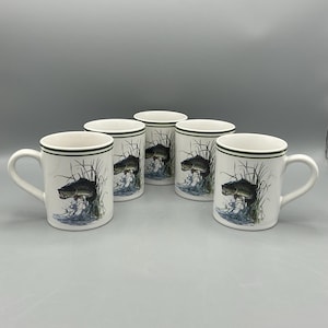 May include: Five white ceramic mugs with a green rim and handle. Each mug features a detailed illustration of a fish jumping out of water, surrounded by reeds. The mugs are arranged on a light gray surface.