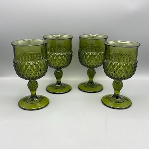 May include: Four green-tinted glass goblets. Each goblet features a diamond-patterned bowl, a stem, and a circular base. The goblets are arranged on a white surface, showcasing their design and color.