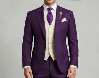 May include: A formal purple suit with a matching vest, white dress shirt, and purple tie. A gold lapel pin and pocket square add detail. The suit is tailored and worn by a person. The brand "NOIR TUXEDOS" is visible.