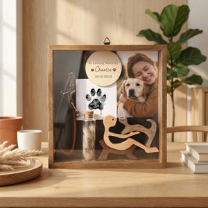 Może przedstawiać: Drewniane pudełko z cieniem z szklanym frontem, zawierające zdjęcie osoby z psem, odcisk łapy, małą fiolkę i drewnianą wycinankę. Pudełko zawiera napis "In Loving Memory Charlie 2010-2023".