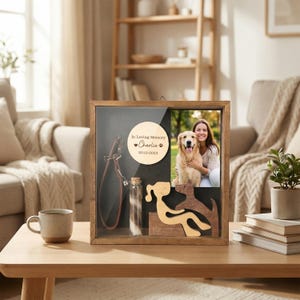Op de afbeelding: Een houten herinneringsdoos met een glazen voorkant, met een foto van een persoon met een hond, een hondenriem, een glazen flesje en een houten silhouet van een hond. De doos bevat een houten schijf met de tekst "In Loving Memory Charlie 2010-2023."