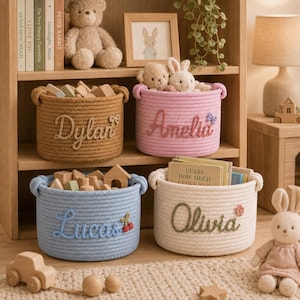 May include: Four round woven rope storage baskets in tan, pink, blue, and cream. Each basket features a personalised name embroidered on the front: Dylan, Amelia, Lucas, and Olivia, accompanied by small decorative icons like a bow, flower, or cherries.