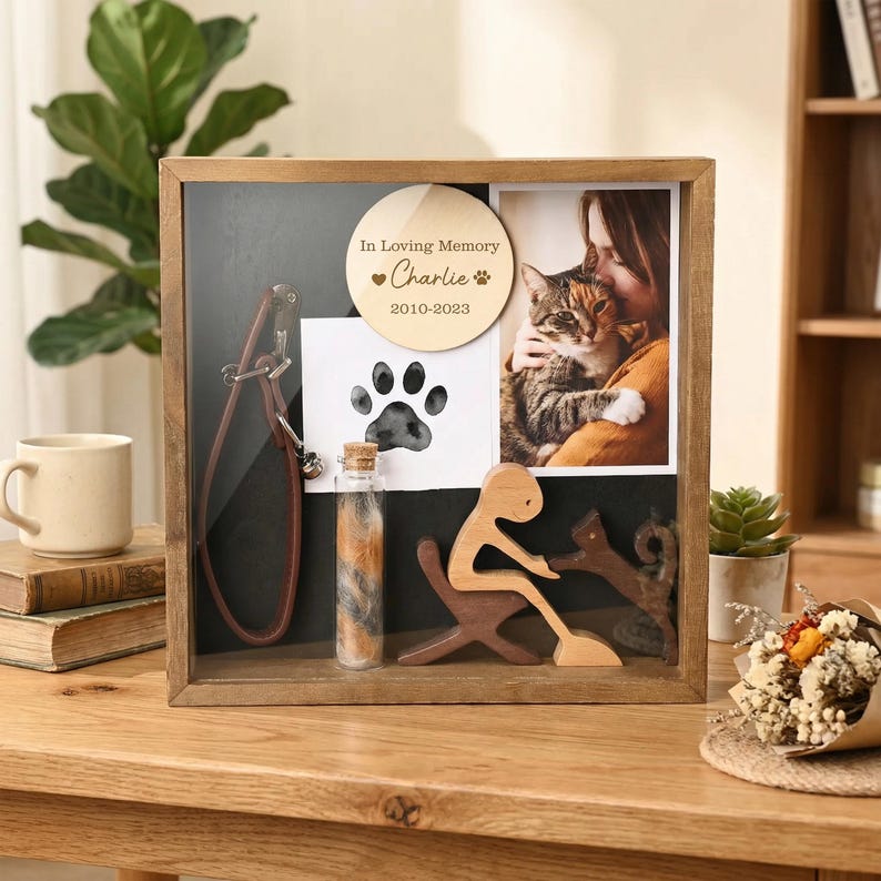 Op de afbeelding: Een houten herdenkingsdoos voor huisdieren. Het bevat een foto, een pootafdruk, een klein flesje met vacht, een houten figuur en een leren halsband. De houten cirkel luidt "In Loving Memory Charlie 2010-2023".