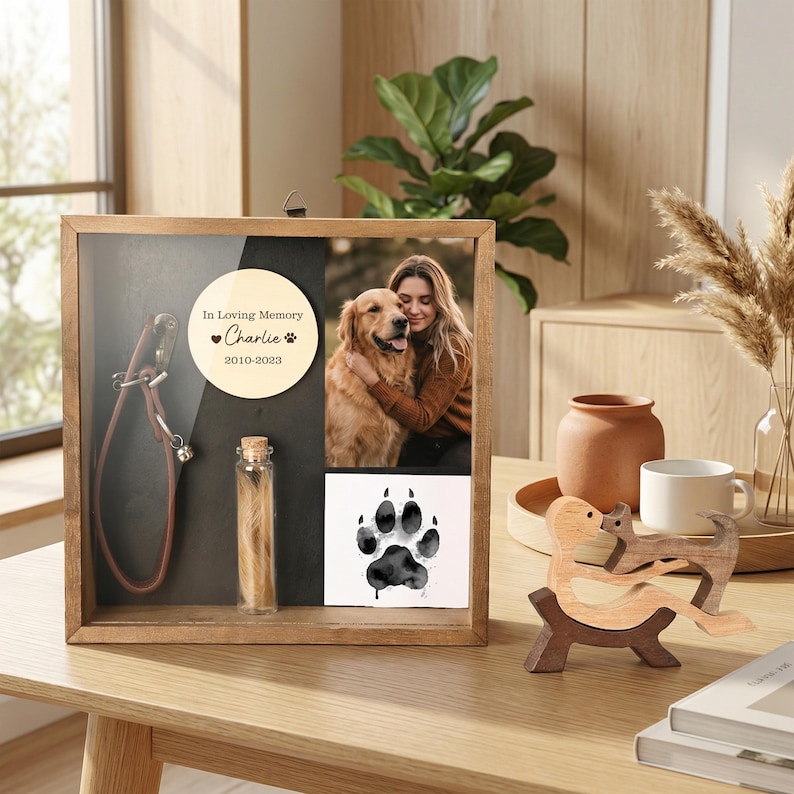 Op de afbeelding: Een houten herdenkingsdoos met een foto van een persoon en een golden retriever, een hondenriem, een klein flesje haar en een pootafdruk. De tekst op de doos luidt "In Loving Memory Charlie 2010-2023."