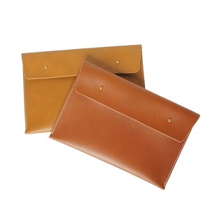 May include: Two leather envelopes, one brown and one tan, with a flap closure and brass accents.