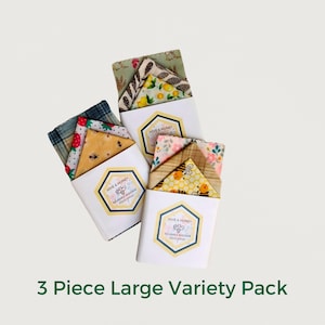 May include: Three beeswax food wraps in a variety pack. The wraps are large and feature different designs with bees, flowers, and geometric patterns. The wraps are packaged in white boxes with the brand name "Hive & Honey" printed on them.