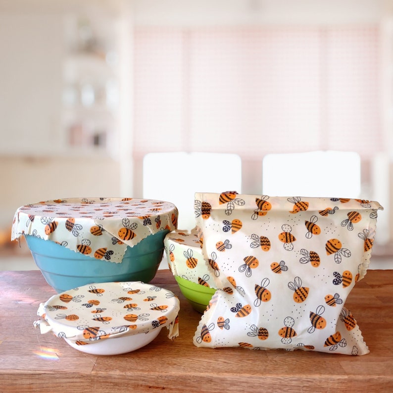 Beeswax food wrap. This 4 piece listing includes a 8" x 8" wrap, 10" x 10" wrap, 12" x 12" wrap and a 8" x 10" baggie. The pattern on this 100% cotton fabric is happy honeybee in flight.