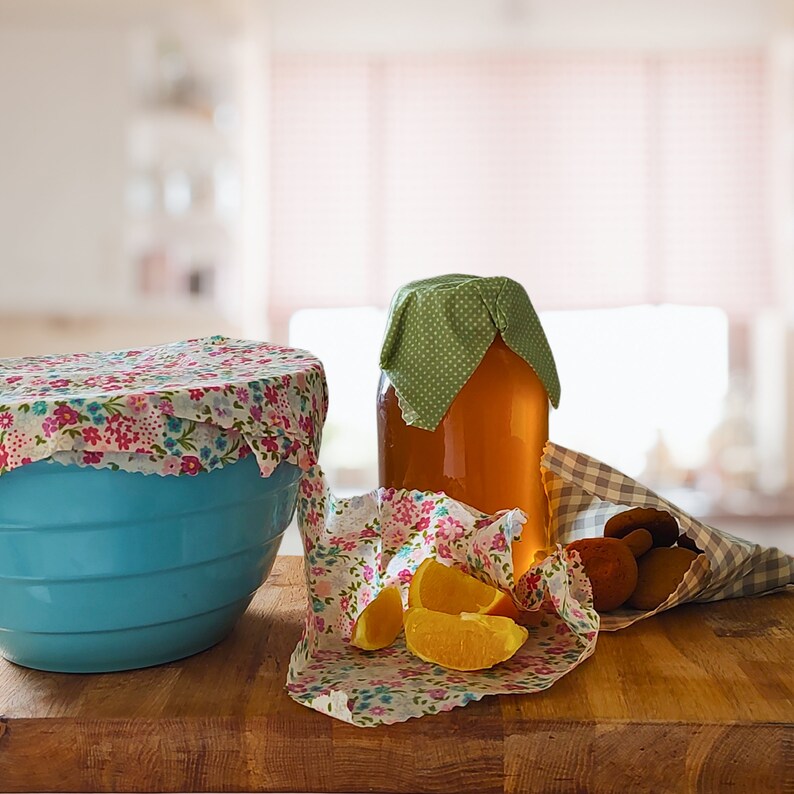 May include: A blue bowl with a floral patterned fabric cover, a glass jar with a green fabric cover filled with honey, and a floral patterned fabric with orange slices on a wooden surface.