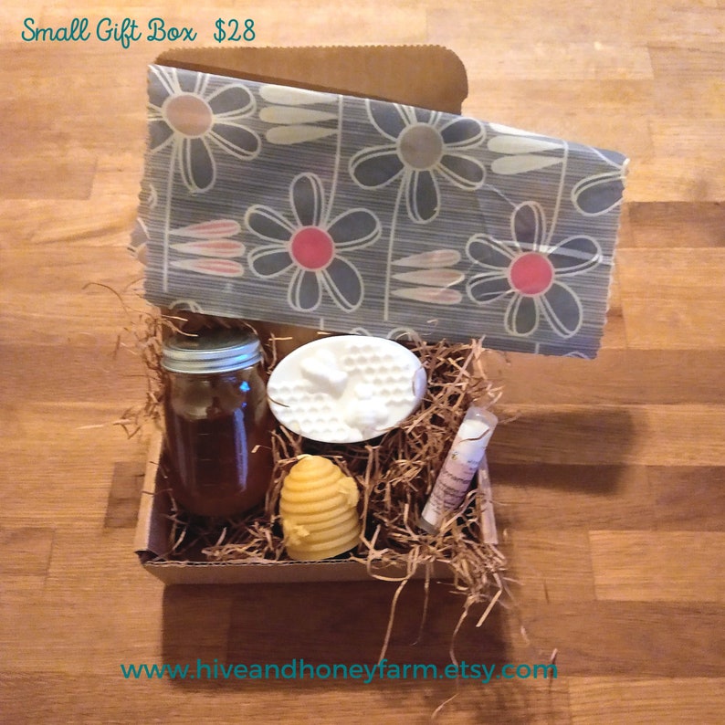 a craft brown gift box containing a jar of honey, lip balm, hive shaped beeswax candle, beeswax food wrap and a oval shaped goats milk soap with a honeycomb and bee imprint