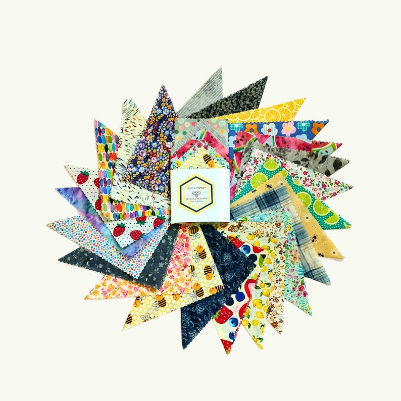May include: A set of 20 colorful reusable food wraps made of beeswax, organic cotton, and tree resin. The wraps are arranged in a circle with a small box in the center that says "Hive & Honey Reusable Food Wraps".