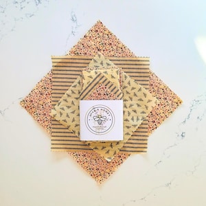 May include: An overhead shot of several reusable food wraps in various patterns. The wraps include floral, striped, and bee designs. A white square card with the text "Hive & Honey" and a bee illustration is centered.