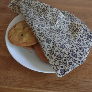 May include: A stack of chocolate chip cookies wrapped in a floral patterned beeswax food wrap. The wrap is beige with a dark brown floral pattern.