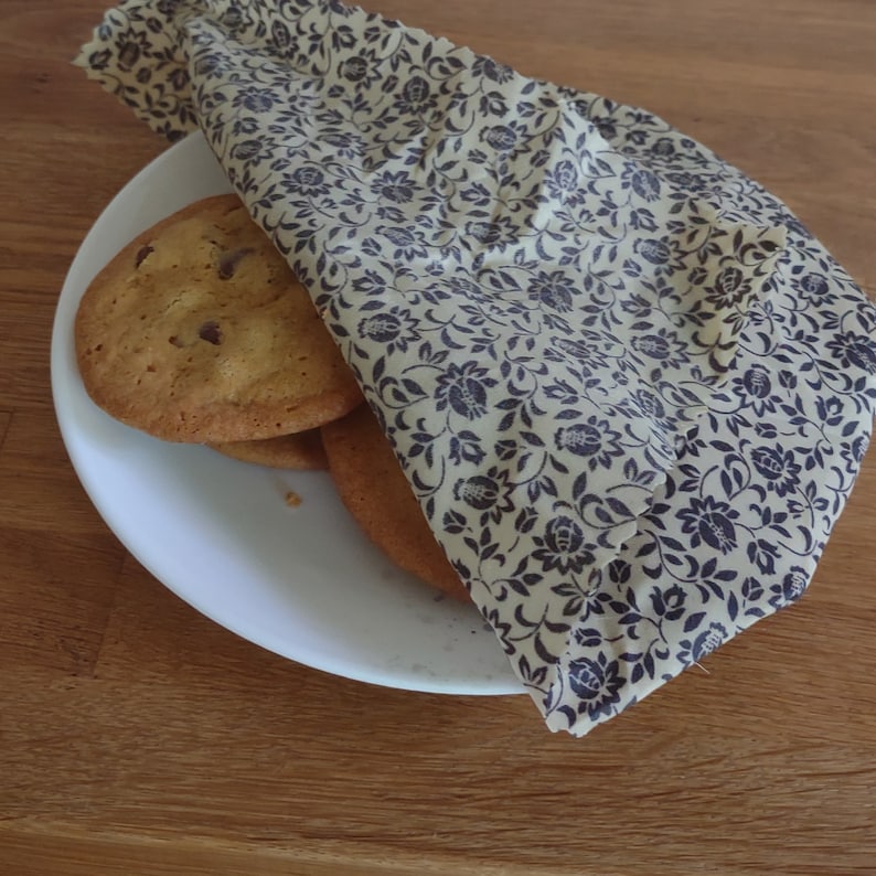 May include: A stack of chocolate chip cookies wrapped in a floral patterned beeswax food wrap. The wrap is beige with a dark brown floral pattern.