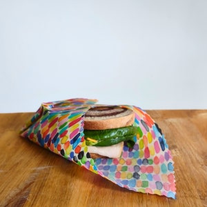 May include: A colorful patterned reusable food wrap with a sandwich inside. The wrap is made of a fabric-like material and has a variety of colors and shapes.