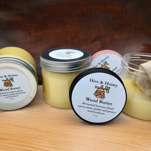 May include: Three glass jars of wood butter, a natural beeswax blend for cleaning, polishing, and protecting wood surfaces. The jars are labeled "Hive & Honey Wood Butter" and have a beehive logo. The jars are 2 oz and 6 oz.