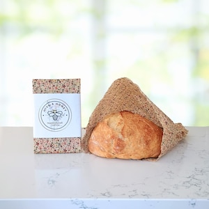 May include: A loaf of bread wrapped in a floral patterned cloth, next to a rectangular box with the text "Hive & Honey" and a bee logo. The box and cloth have a similar floral design.