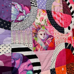 Puede incluir: Una colcha de retazos colorida con una variedad de telas y patrones, incluyendo c&iacute;rculos, estrellas y dise&ntilde;os florales. La colcha est&aacute; hecha de muchos colores diferentes, incluyendo rosa, morado, negro y blanco.