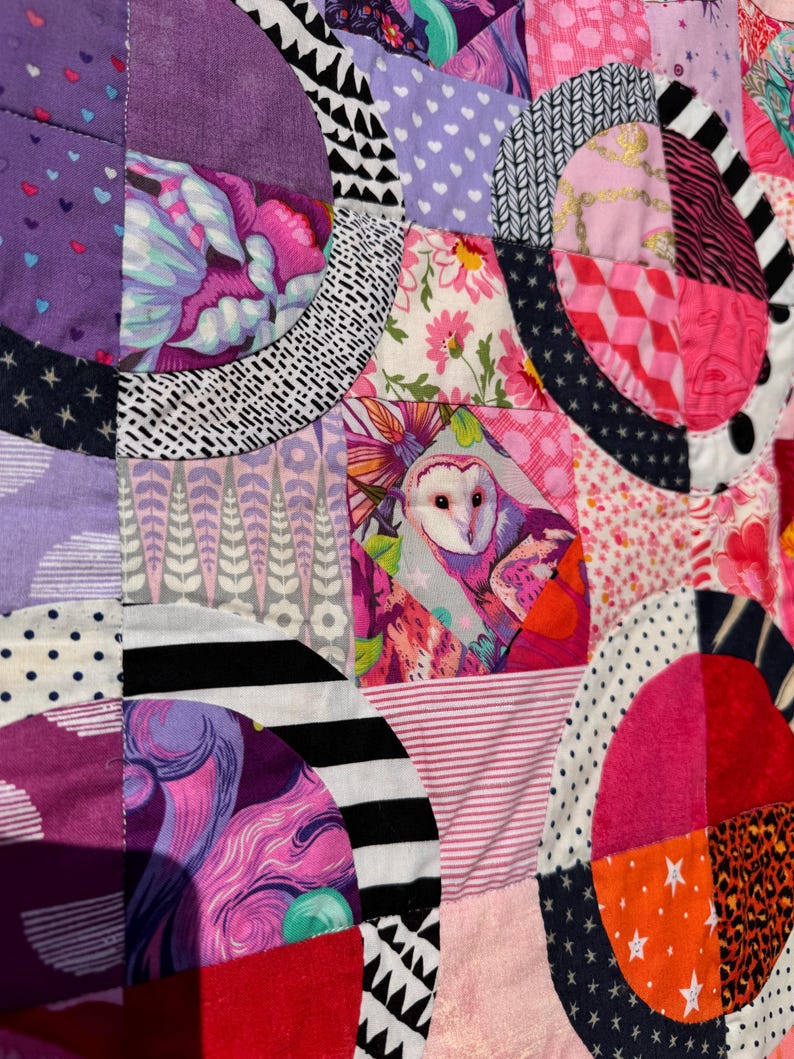 Puede incluir: Una colcha de retazos colorida con una variedad de telas y patrones, incluyendo c&iacute;rculos, estrellas y dise&ntilde;os florales. La colcha est&aacute; hecha de muchos colores diferentes, incluyendo rosa, morado, negro y blanco.