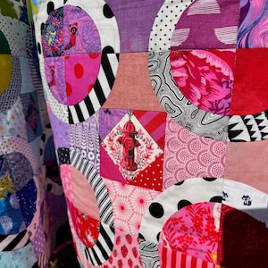 Puede incluir: Una colcha de retazos colorida con una variedad de patrones y colores, incluyendo rosa, rojo, negro, blanco y azul. La colcha est&aacute; hecha de cuadrados y c&iacute;rculos, y presenta un dise&ntilde;o de hidrante de incendios en el centro.