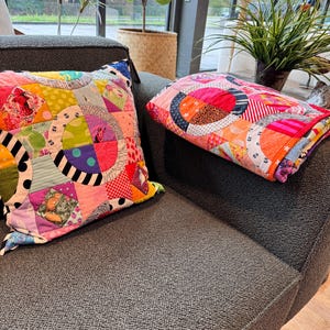 Puede incluir: Dos almohadas de patchwork coloridas con un patr&oacute;n circular en tonos de rosa, rojo, amarillo, verde, azul y negro. Las almohadas est&aacute;n en un sof&aacute; gris.