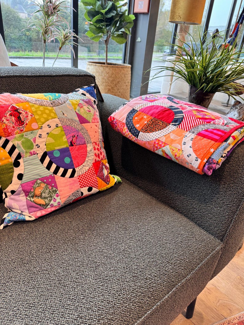 Puede incluir: Dos almohadas de patchwork coloridas con un patr&oacute;n circular en tonos de rosa, rojo, amarillo, verde, azul y negro. Las almohadas est&aacute;n en un sof&aacute; gris.
