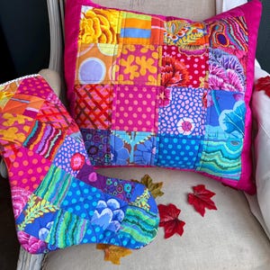 Puede incluir: Un cojín cuadrado de patchwork y un calcetín acolchado a juego que presentan una vibrante variedad de cuadrados de tela coloridos con patrones florales, de lunares, de cuadros y abstractos en tonos rosa, azul, amarillo, naranja y verde con bordes rosas.