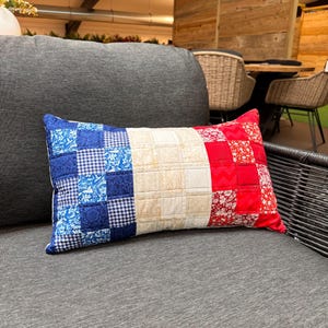 May include: A rectangular pillow with a patchwork design featuring the colors of the French flag: blue, white, and red. The pillow is made of fabric with a checkered pattern and floral designs.