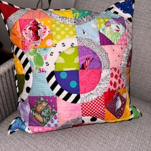 Puede incluir: Una almohada de patchwork colorida con una variedad de patrones y colores, incluyendo rojo, amarillo, verde, azul y rosa. La almohada est&aacute; hecha de cuadrados de tela cosidos juntos en un dise&ntilde;o geom&eacute;trico.
