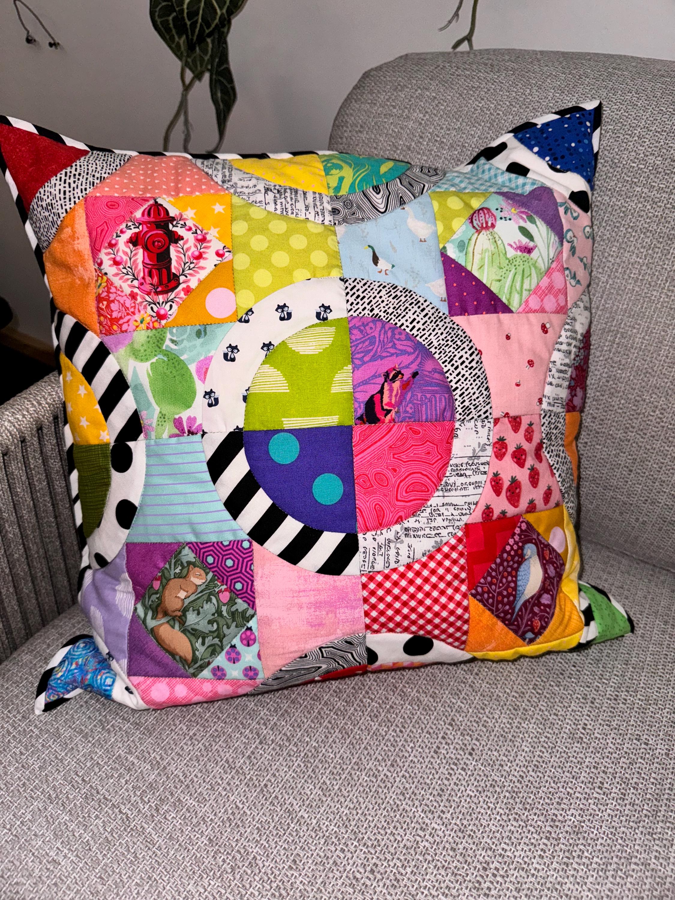 Puede incluir: Una almohada de patchwork colorida con una variedad de patrones y colores, incluyendo rojo, amarillo, verde, azul y rosa. La almohada est&aacute; hecha de cuadrados de tela cosidos juntos en un dise&ntilde;o geom&eacute;trico.