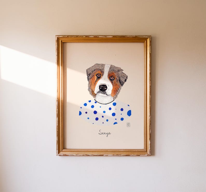 May include: A framed watercolor portrait of a dog with brown, white, and gray fur. The dog is wearing a white shirt with blue polka dots. The name "Senya" is written below the dog's portrait in cursive.