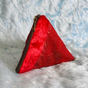 May include: A red triangular pouch with a gold key-shaped zipper pull. The pouch is made of red velvet and a red fabric with gold flecks. The zipper is brown.