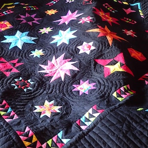 Könnte beinhalten: Eine schwarze Steppdecke mit verschiedenen bunten sternförmigen Mustern. Die Steppdecke ist mit einem wirbelnden Muster gesteppt.